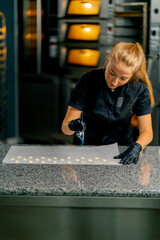 A confectioner squeezes chocolate from a pastry bag in the form of natural candies onto parchment in pastry shop