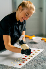 A confectioner squeezes chocolate from a pastry bag in the form of natural candies onto parchment in pastry shop