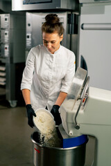 A female baker in  white chef's tunic kneads dough to prepare and bake bread in the bakery
