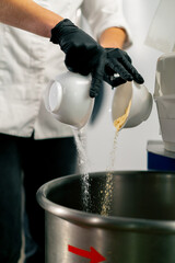 A close-up of a female baker in a white chef's tunic pouring flour to prepare and bake bread in bakery
