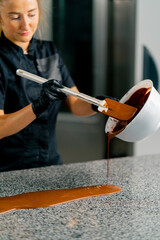 Close-up shot of a chocolatier mixing chocolate in bowl and preparing it for tempering for making...