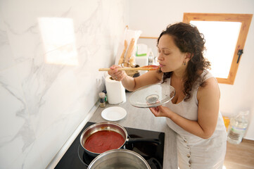 Young Latin American pretty housewife tasting the tomato sauce she's cooking in the home kitchen