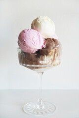 Vanilla, chocolate and strawberry ice cream scoops in glass on white background