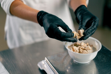 Close-up shot of female hands in gloves breaking yeast to prepare dough for baking bread in bakery - obrazy, fototapety, plakaty