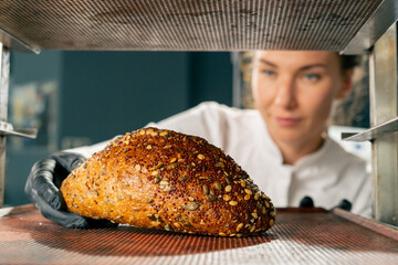A female baker wearing gloves takes out a baking sheet with freshly baked hot bread from oven