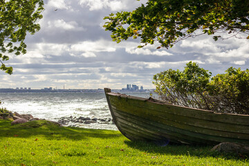 
The bow of a wooden boat on the shore against the background of the city and the sea