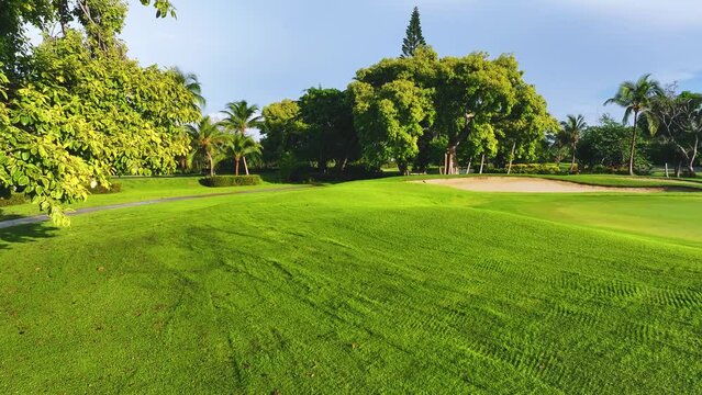 Short cut grass lawn in a tropical golf park and blue sky. Outdoor sport and lifestyle concept. Landscape of a golf course. A green lawn and a beautiful view of the sky over a lawn with palm trees.