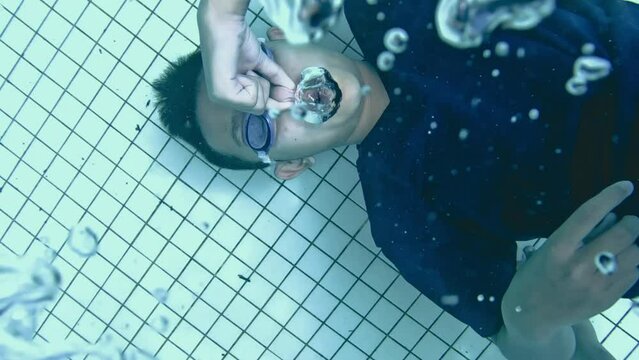 A young boy blows ring bubbles underwater in the swimming pool. 4K in slow motion