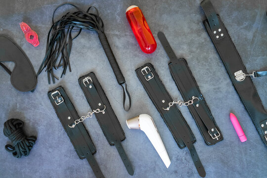  A set of erotic toys for BDSM (ball gag, cuffs, rope, flogger, collar and leash) for BDSM fantasy games and fastenings on a gray concrete background. Intimate sex games. 