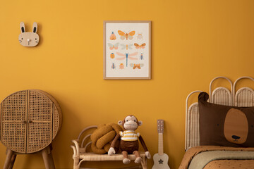 Aesthetic composition of child room interior with mock up poster frame, yellow wall, plush toys, monkey, rattan sideboard, guitar, brown bedding and personal accessories. Home decor. Template. - obrazy, fototapety, plakaty