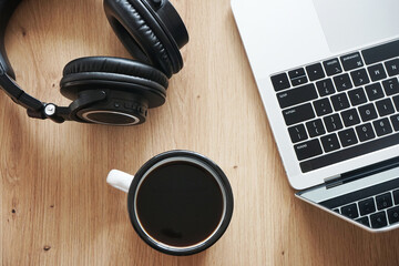 Black headphones, a cup of coffee and an open laptop next to each other on a wooden table