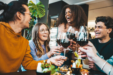 Multiracial group of friends toasting red wine sitting at bar restaurant table - Millennial people...