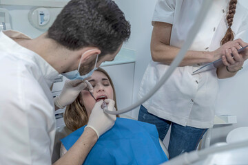 he dentist makes a professional cleaning of the teeth of a young female patient in the dental office.