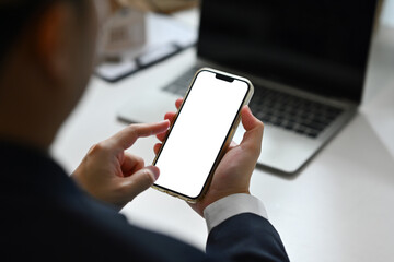 Over shoulder view of male manager using smartphone at desk