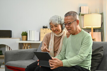 Happy senior couple spending time together at home and using digital tablet for surfing internet or shopping online