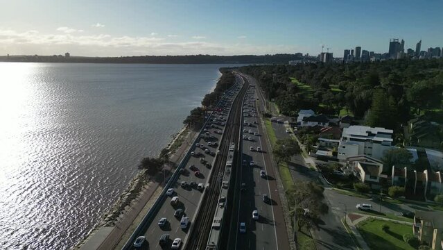 Traffic car along State Route 2 and train passing at sunset, Swan river at Perth in Australia. Aerial drone view and slow-motion