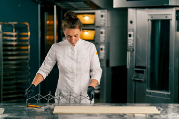 Woman chef stands at the kitchen table with dough divider and cuts the dough into equal parts for making croissants