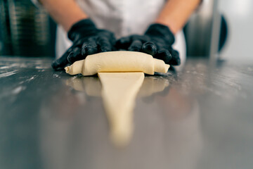 Close-up of the chef's gloved hands shaping and twisting raw dough into shape of croissants for...