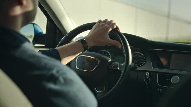 An unrecognizable man is driving his car. The shot shows hands on the steering wheel, the dashboard and the street.