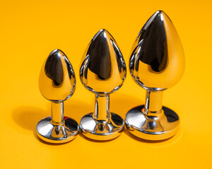 Three size steel butt plugs on an orange background.