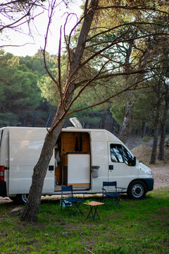 Parked camper van under tree with camp table and chairs in countryside