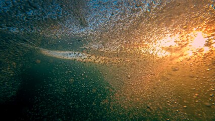 Underwater shot of sunset sun rays shining through sea water waves. Air bubbles rising up