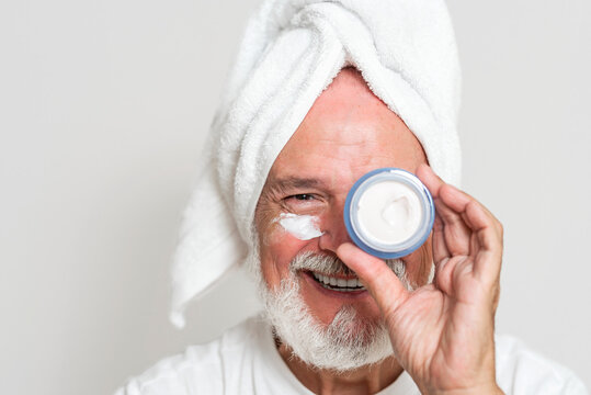 Happy senior man showing jar with cream after bath