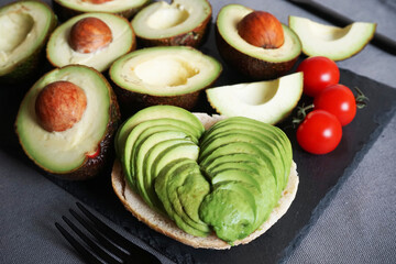 A lot of sliced ​​avocado next to cherry tomatoes, fork and knife on a gray background