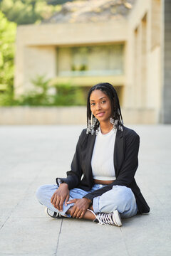 Smiling African American female sitting on floor in yard of building