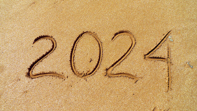 2024 written on the sea sand. Sandy textured background. Close-up view. Travel concept of relax vacations in a New year. Template for greeting card, postcard, invitation, promotion materials, websites