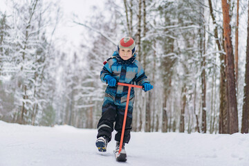 Fototapeta na wymiar winter activities with kids. little boy wearing overall ride kick ski sled