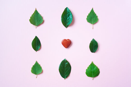 Red heart stone toy heart on a kraft pink paper background. Heart shape in fresh green leaves. Valentine in eco-friendly vegan style. Valentine's Day concept. I love nature. I love forest.