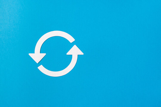 Recycling symbol cut out of white paper on blue background, top view. Concept of ecology and paper recycling. Recycled. Eco arrow reuse material.