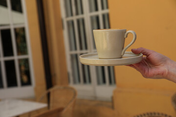 Cup in hand on orange wall background in cafe, space for text