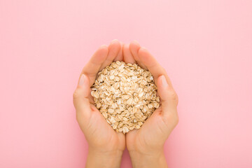 Young adult woman hands holding dry rolled oat on light pink table background. Pastel color....