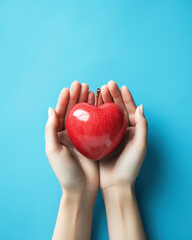 Woman's hands holding a heart shaped fresh red apple on light azure or blue background. Food charity or fight with hunger conceptual image