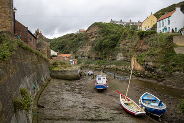 Boats in tidal river mouth on dry bed in Yorkshire valley coastal town 