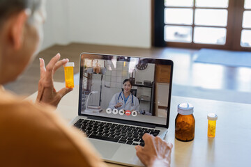 Older woman is making video call with doctor on laptop and consulting about medicine