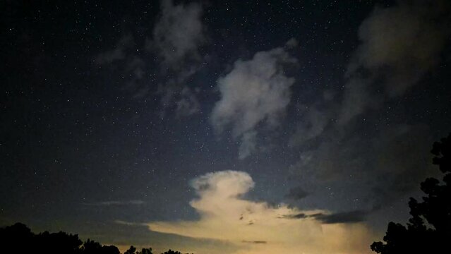 Late night time lapse of clouds rolling against starry sky