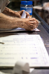 Naklejka premium Close-up of a hand holding a pen in a book. Hand of aged man doing accounting work manually. Active aging concept, handwriting. Vertical image.
