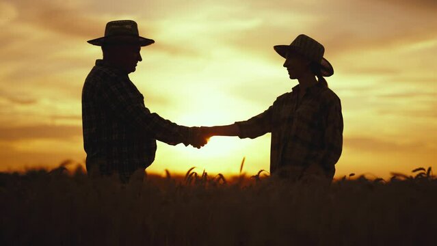 Silhouette of farmers senior man young woman shaking hands concluding business contract on agricultural field at sunset. Cooperation on farm, partnership, collaboration. Farming, agribusiness concept.