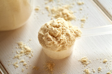 Whey protein powder in a plastic scoop on a white table