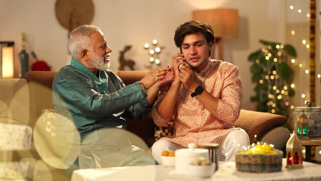 Indian father and son talking on phone on diwali while both are sitting on the sofa.they both are very happy.father happily snatching the phone from his son to talk.hindu festival concept.