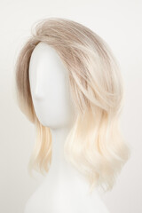 Natural looking blonde fair wig on white mannequin head. Middle length hair cut on the plastic wig holder isolated on white background.