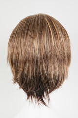 Fototapeta premium Natural looking dark brunet wig on white mannequin head. Short brown hair on the plastic wig holder isolated on white background, back view.