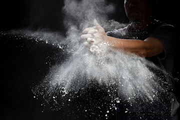 Chef prepare white flour dust for cooking bakery food. Elderly man Chef clap hand, white flour dust explode fly in air. Flour stop motion in air with freeze high speed shutter, black background - obrazy, fototapety, plakaty