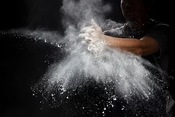 Poster Chef prepare white flour dust for cooking bakery food. Elderly man Chef clap hand, white flour dust explode fly in air. Flour stop motion in air with freeze high speed shutter, black background © Jade