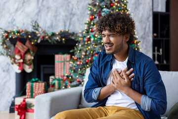 A sick man is sitting at home in the living room on the sofa for Christmas. A Latin American has...