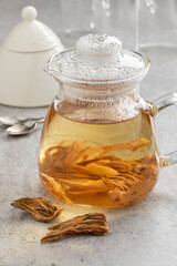 Glass teapot with white hibiscus leaves and a heap of dried leaves in front close up