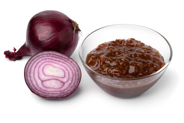 Glass bowl with caramelized red onion chutney and a fresh red onion on the side close up isolated...